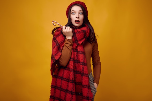 Beautiful brunette woman in red hat with big knitted scarf holding a candy