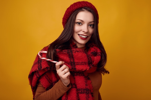 Beautiful brunette woman in red hat with big knitted scarf holding a candy