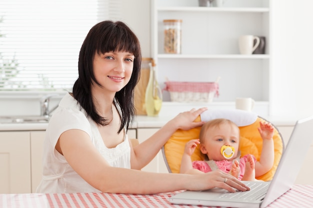 Beautiful brunette woman relaxing with her laptop next to her baby while sitting