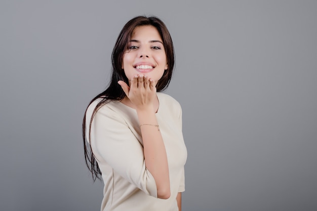 Beautiful brunette woman smiling sending a kiss isolated over grey