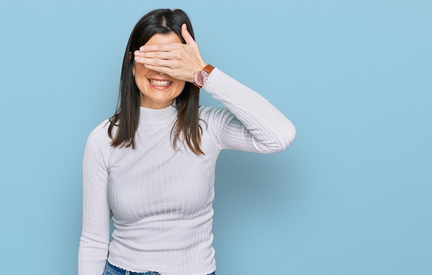 Beautiful brunette woman wearing casual clothes smiling and laughing with hand on face covering eyes for surprise blind concept