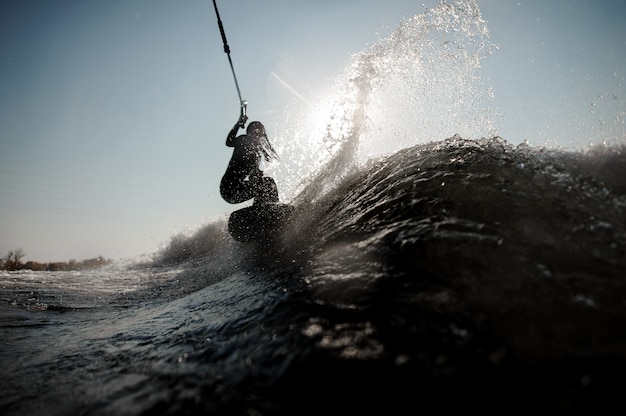 Beautiful brunette woman in the white swimsuit jumping on the green wakeboard holding a rope