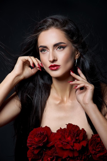 Beautiful brunette woman with a bouquet of red rose flowers in red corset. Long hair, nude slim body art portrait