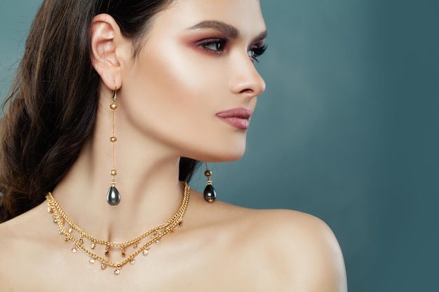 Beautiful Brunette Woman with Gold Jewelry and Black Pearls Earrings Cute Female Model on Blue Background