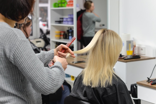 Beautiful brunette working as a hairdresser cuts the ends of the client's hair in a beauty salon