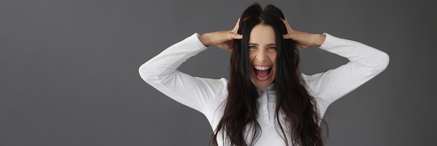 A beautiful brunette yells holding her head closeup concept stress negative emotions critical