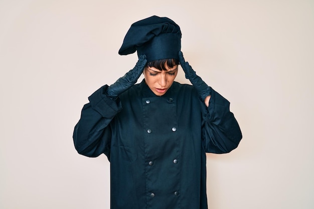 Beautiful brunettte woman wearing professional cook uniform with hand on head for pain in head because stress suffering migraine