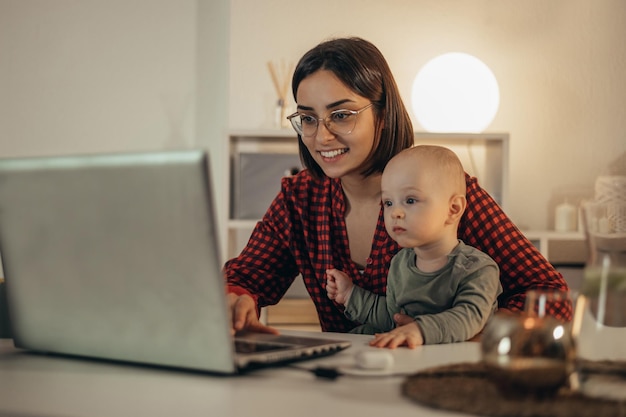 Beautiful business mom using a laptop and spending time with her baby boy at home