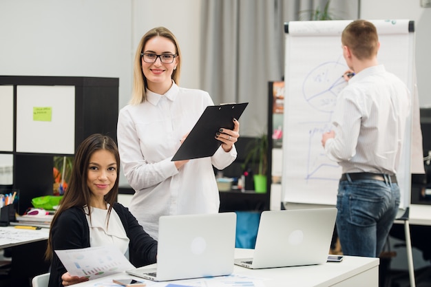 Beautiful business people are looking at camera and smiling while standing in office