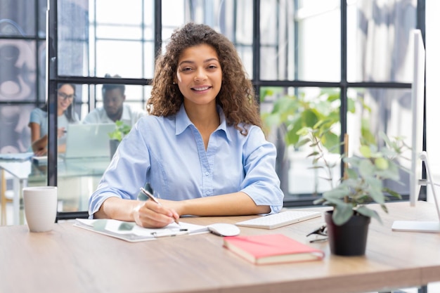 Beautiful business woman is examining documents while sitting in the office Collegues are on the background