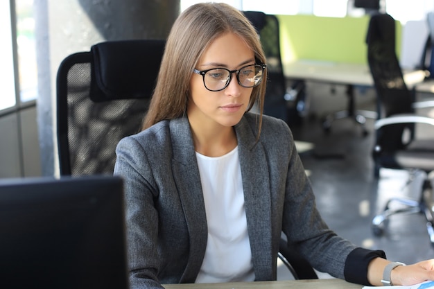 Beautiful business woman is examining documents while sitting in the office.