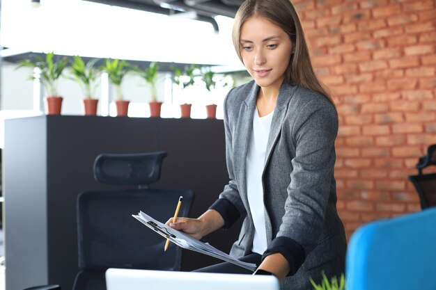 Beautiful business woman is examining documents while working in the office.