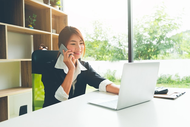 Beautiful business woman talking on the cellphone working with laptop and calculator 