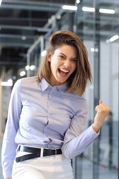 Beautiful businesswoman is keeping arm raised and expressing joyful in office