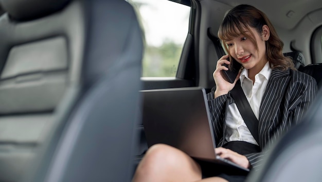 Beautiful businesswoman using laptop and mobile phone while sitting on a backseat of a car