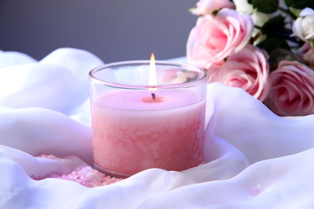 Beautiful candle with flower on white cloth, close up