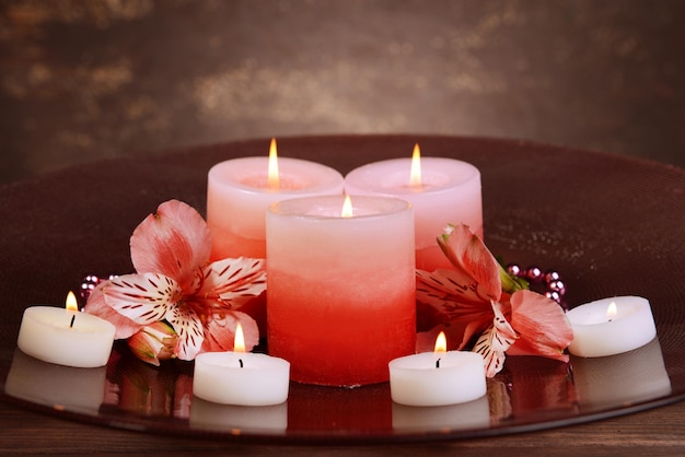 Beautiful candles with flowers on table on brown background