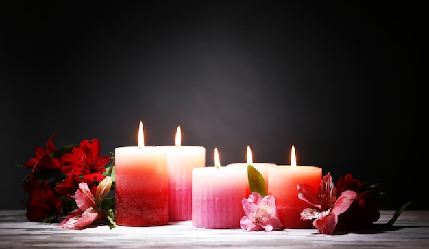 Beautiful candles with flowers on wooden table, on dark background