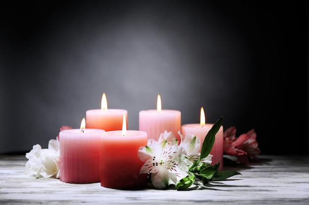 Beautiful candles with flowers on wooden table, on dark background