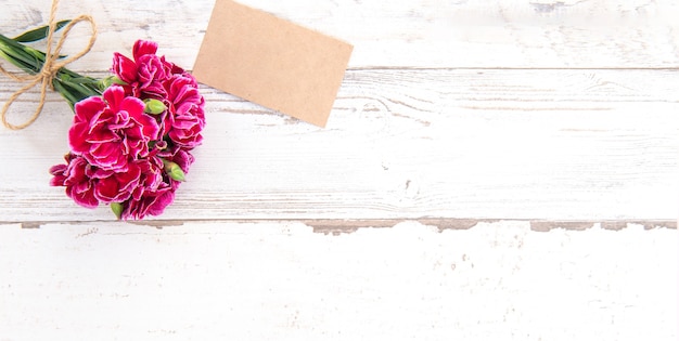 Beautiful carnations with template card isolated on a bright wooden table, copy space, flat lay, top view