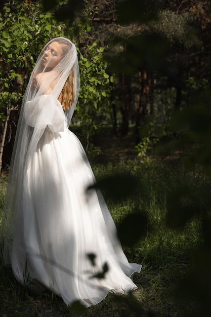 Beautiful caucasian blonde girl in a wedding dress under a veil in the sunlight in the forest wedding image of the brides