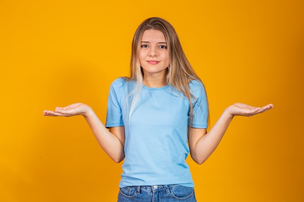 Beautiful caucasian blonde woman wearing casual blue t shirt clueless and confused expression with arms and hands raised. doubt concept.