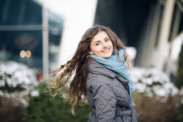 Beautiful caucasian elegant girl with beautiful curly brown hair walks happy in downtown.