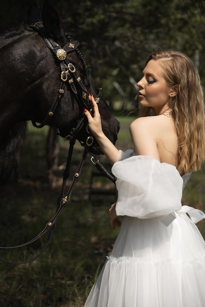 Beautiful caucasian girl in a wedding dress strokes a horse in the face