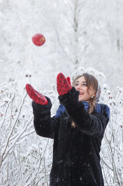 Beautiful caucasian girl with chestnut hair plays with red apple among branches covered with frost