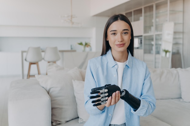 Beautiful caucasian girl with disability taking apart her bionic prosthetic arm standing at home