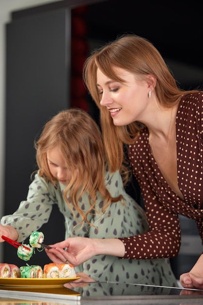 Beautiful caucasian mom and daughter eating rolls and sushi at family lunch at home Delivery food Traditional japanese food