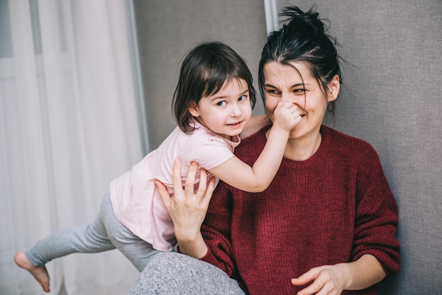 Beautiful Caucasian mother and her child playing together at home Girl and mom in casual sitting on th carpet Happy mum and kid having fun smiling and hugging Family holiday and togetherness