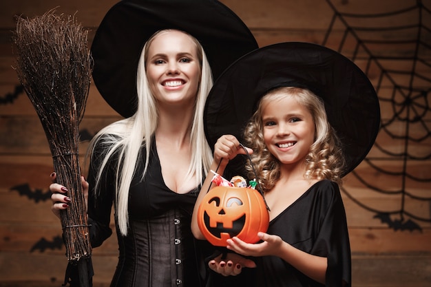 beautiful caucasian mother and her daughter in witch costumes celebrating Halloween with sharing Halloween candy 