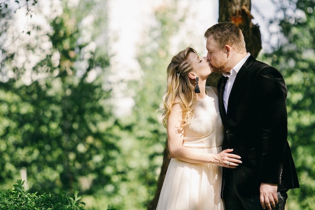 beautiful caucasian newlyweds kiss in the garden against the backdrop of greenery.