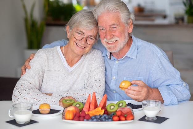 Beautiful caucasian retired senior couple having breakfast at home with fresh seasonal fruit milk and cupcake healthy eating concept