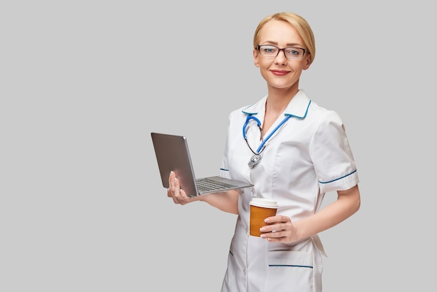 Beautiful Caucasian woman doctor or nurse holding a laptop pc computer and cup of coffee to go