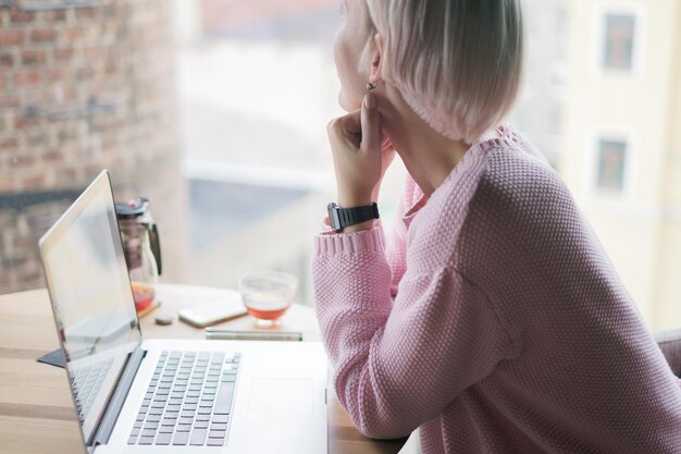 Beautiful caucasian woman dreaming about something while sitting with portable laptop in cafe bar looking away at window