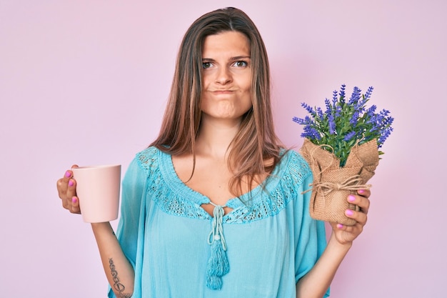 Beautiful caucasian woman drinking a cup of infused lavender skeptic and nervous frowning upset because of problem negative person