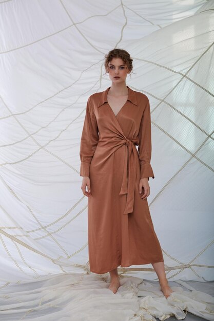 Beautiful caucasian woman in a long dress posing in front of the parachute in the studio.