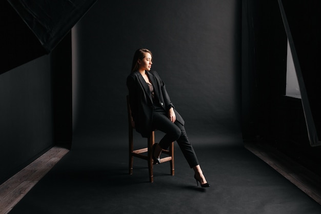 Beautiful caucasian woman sitting on a chair in a photo studio in a black formal suit