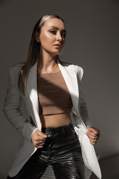 Beautiful caucasian woman in a white jacket black trousers holds a jacket and looks at the camera fashion image