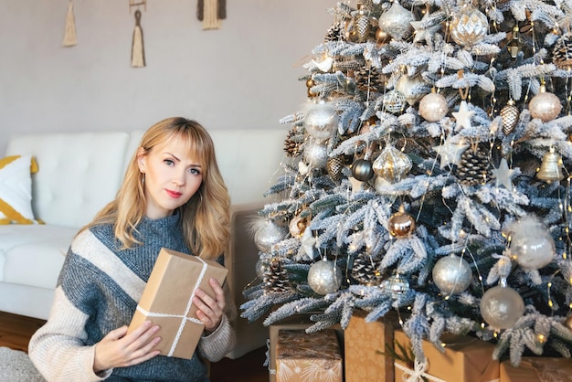 A beautiful caucasian years old woman with a gift in hands posing at christmas tree classic