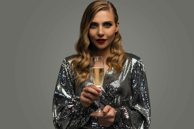 Beautiful celebrating woman holding glass of champagne and smiling isolated over studio background