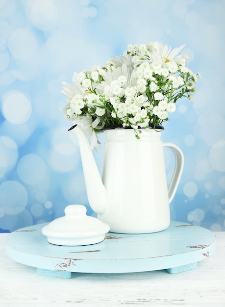 Beautiful chamomiles in teapot on table on bright background