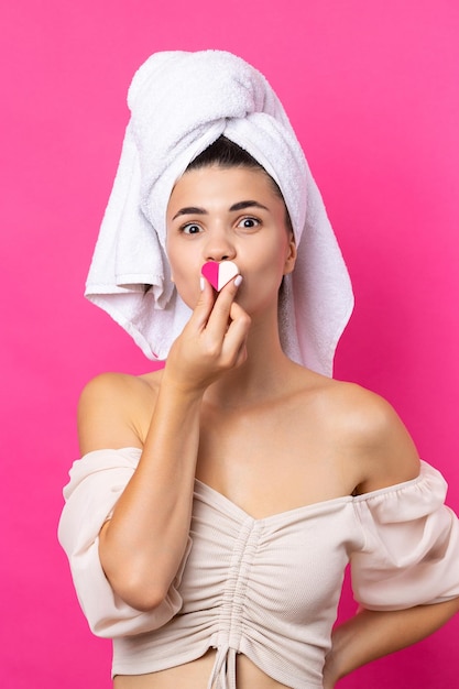 Beautiful cheerful attractive girl with a towel on her head holds a sponge in the form of a pink heart