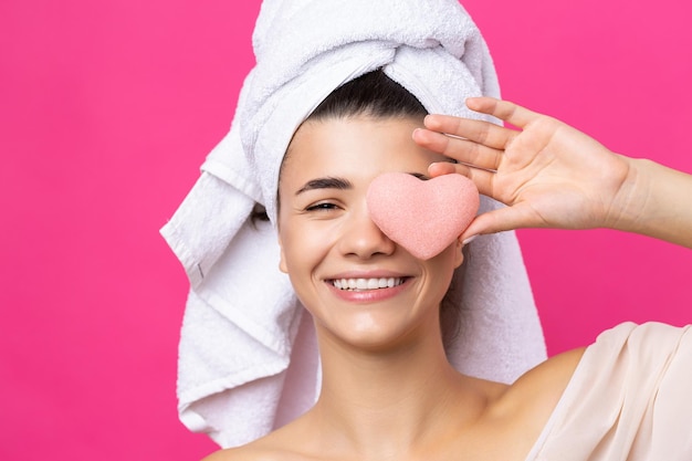 Beautiful cheerful attractive girl with a towel on her head holds a sponge in the form of a pink heart