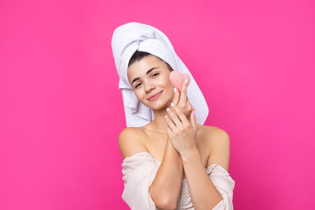 Beautiful cheerful attractive girl with a towel on her head holds a sponge in the form of a pink heart