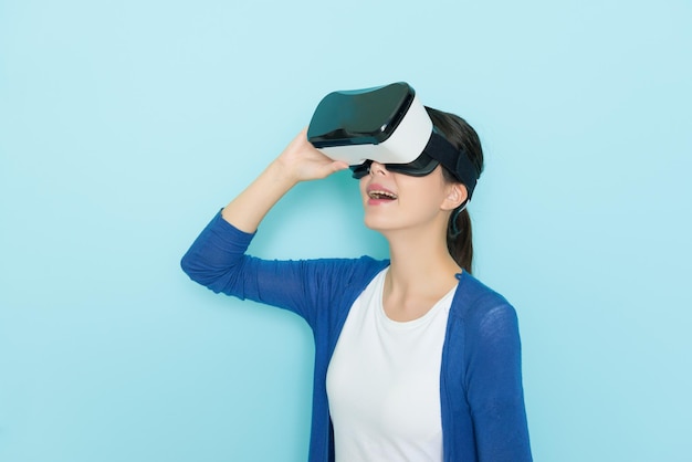 beautiful cheerful girl adjusting VR headset device to browsing online  website and enjoying 3D video in blue background with freedom casual clothing.