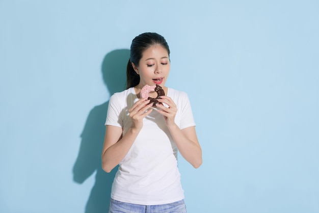 beautiful cheerful girl holding delicious donuts feeling happy and standing on blue wall background ready to eating enjoying dessert.