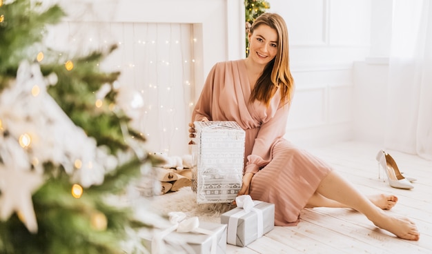 Beautiful cheerful happy young girl with christmas gifts on the of a new year tree at home